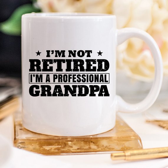 A humorous coffee mug featuring the phrase 'I'm Not Retired, I'm A Professional Grandpa', showcasing a fun design perfect for grandparents.