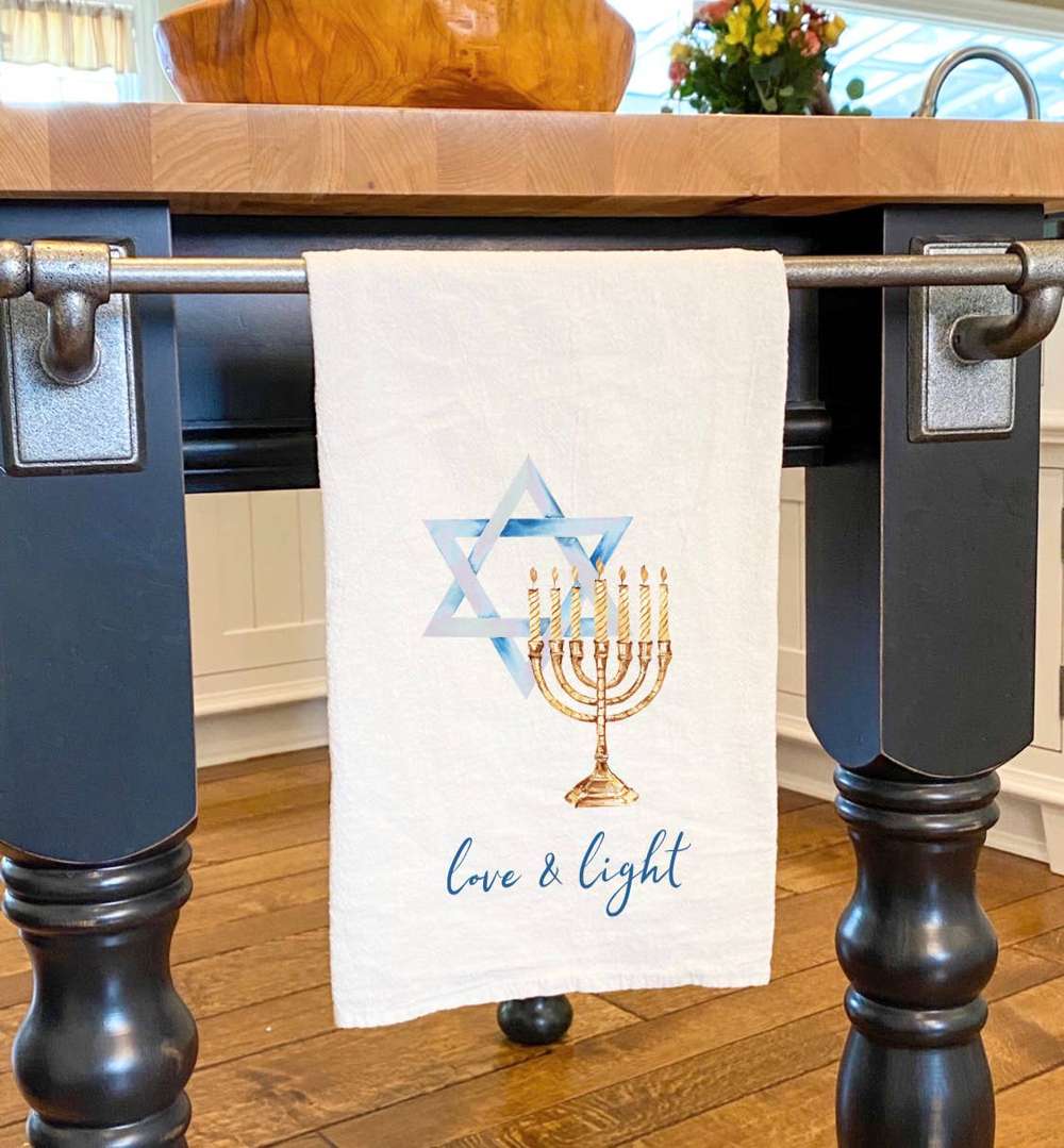 Cotton tea towel featuring a Menorah and Star of David design, vibrant colors, and hemmed edges, perfect for Hanukkah celebrations.