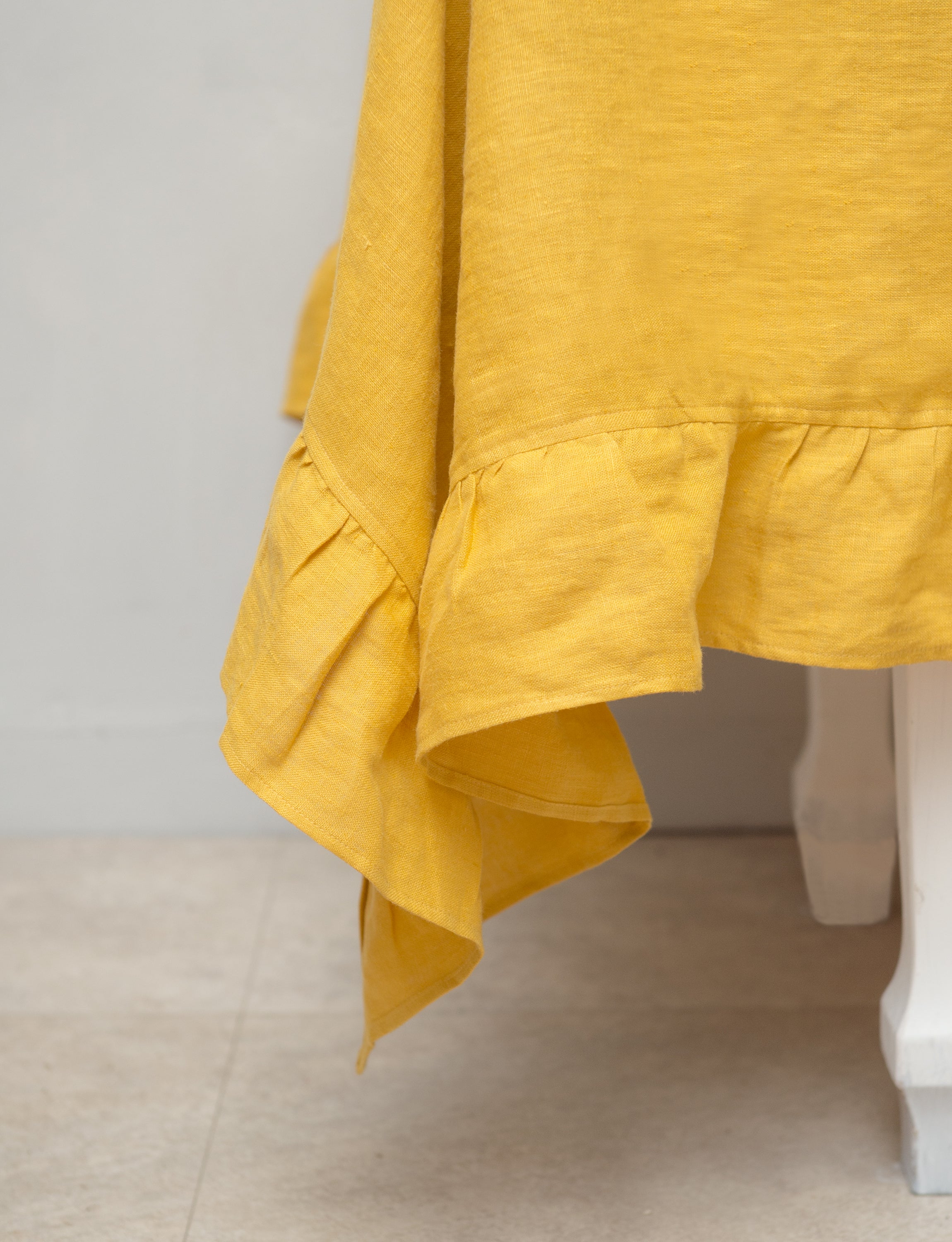 Bright honey-colored linen tablecloth with elegant ruffles, showcasing its luxurious texture and drape.