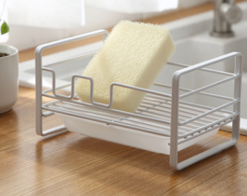 Household rack for kitchen sponges and brushes with a detachable drain basket, featuring a sleek white design and non-slip footpad.