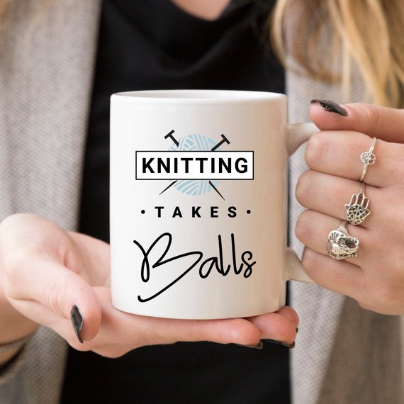 A humorous coffee mug with the phrase 'Knitting Takes Balls', featuring a colorful design perfect for knitting enthusiasts.