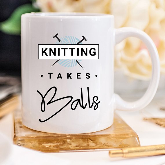 A humorous coffee mug with the phrase 'Knitting Takes Balls', featuring a colorful design perfect for knitting enthusiasts.