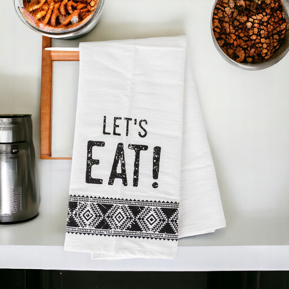 A stylish black and white tea towel featuring an Aztec design with the phrase 'Let's Eat!' printed on it, perfect for kitchen decor.