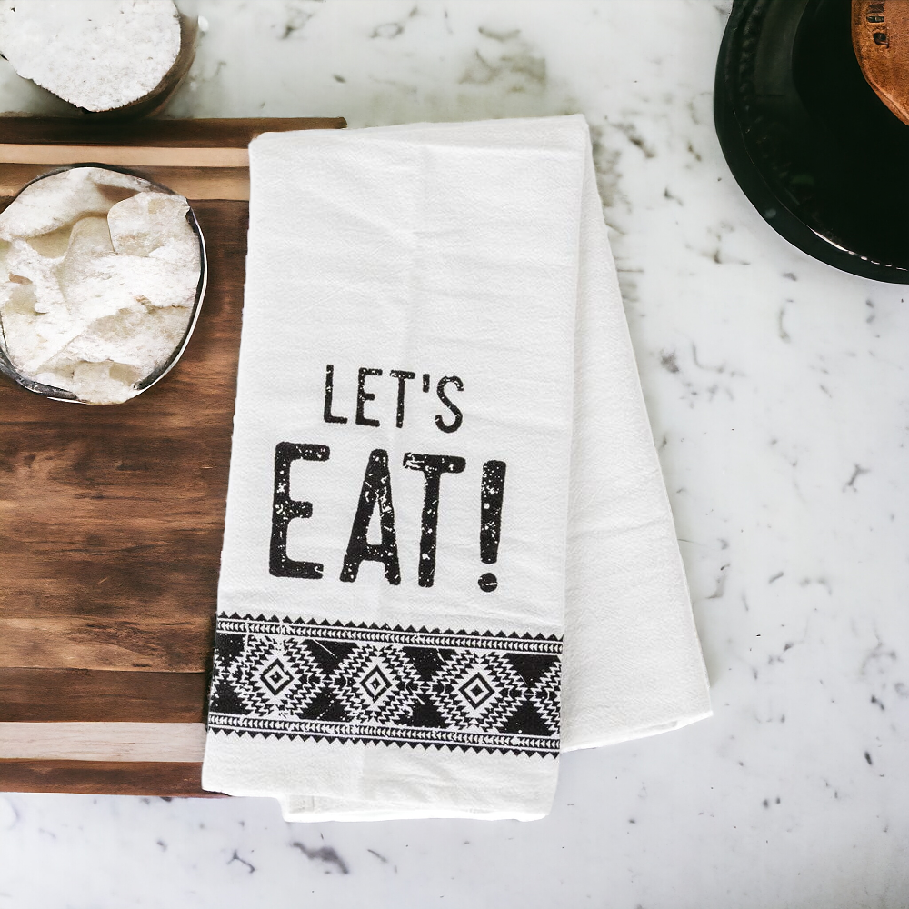 A stylish black and white tea towel featuring an Aztec design with the phrase 'Let's Eat!' printed on it, perfect for kitchen decor.