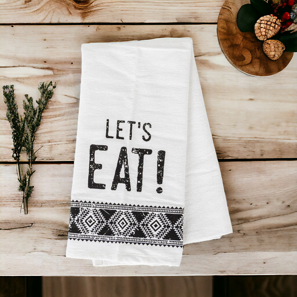 A stylish black and white tea towel featuring an Aztec design with the phrase 'Let's Eat!' printed on it, perfect for kitchen decor.