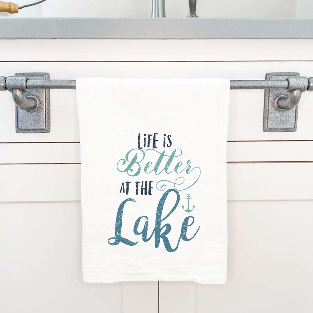 A vibrant cotton tea towel featuring the phrase 'Life is Better at the Lake', showcasing a charming lakeside design, perfect for kitchen use.