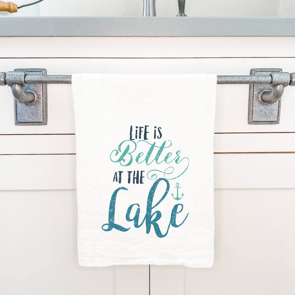 A vibrant cotton tea towel featuring the phrase 'Life is Better at the Lake', showcasing a charming lakeside design, perfect for kitchen use.