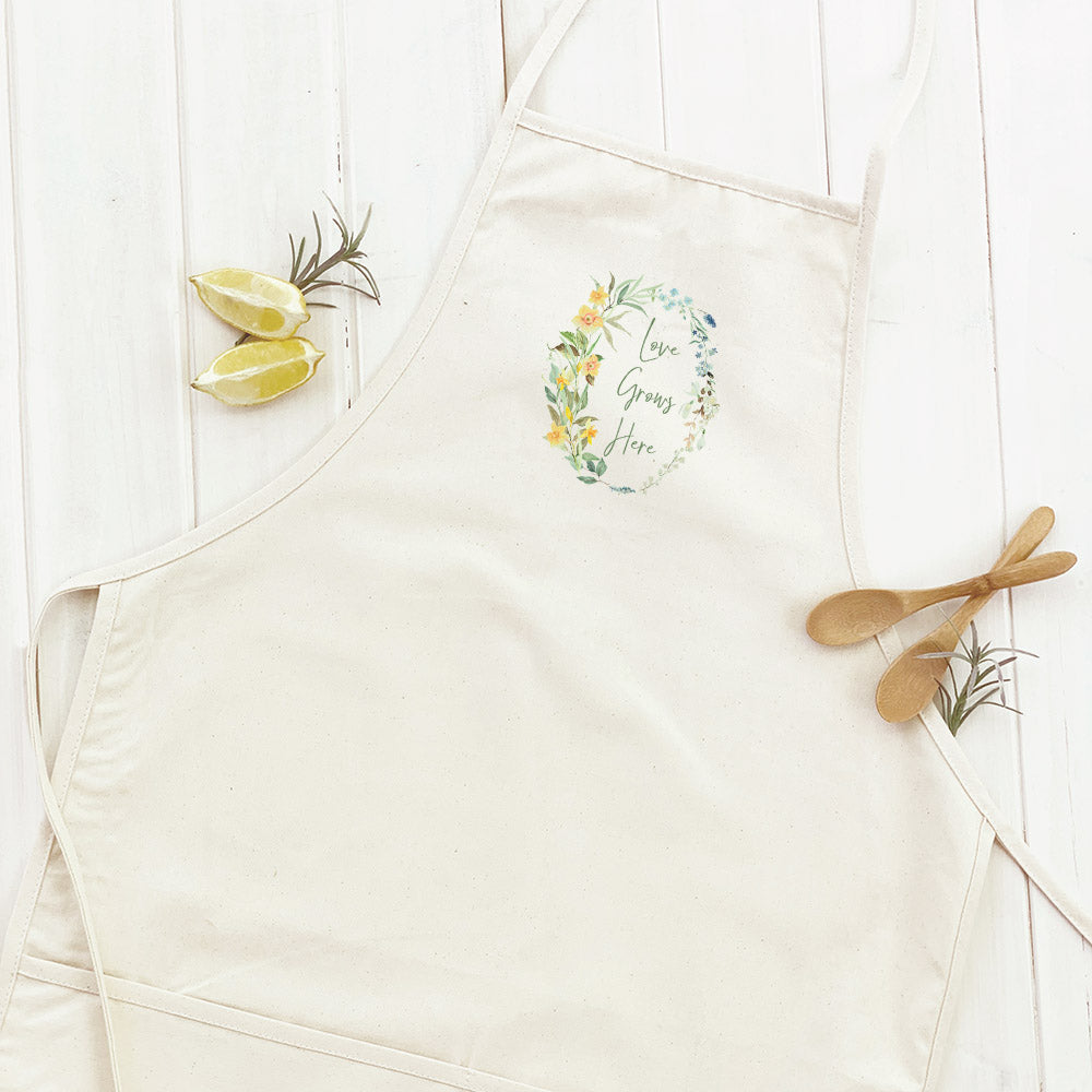 Love Grows Here Wreath Women's Apron featuring elegant design and divided front pocket, made from durable cotton canvas.