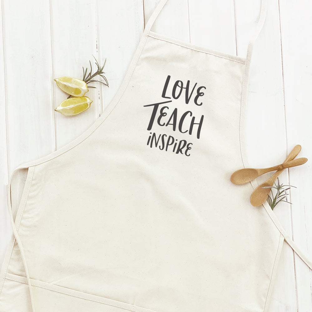 Love Teach Inspire Women's Apron in cotton canvas with adjustable neck and divided front pocket, featuring elegant design and natural twill ties.