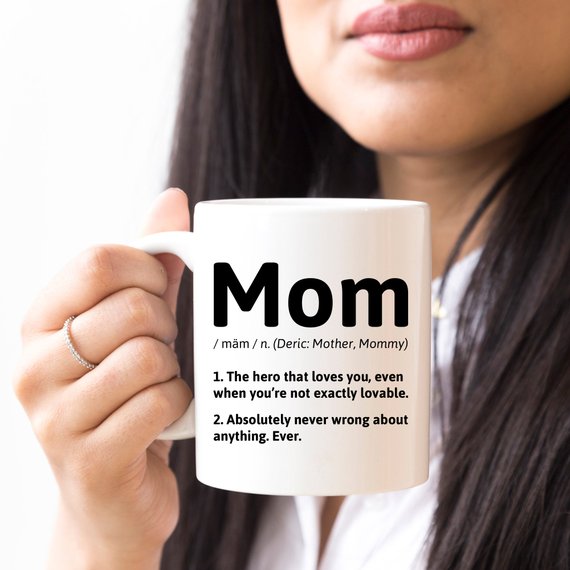 A white ceramic coffee mug featuring a humorous definition of 'Mom', perfect for gifts.