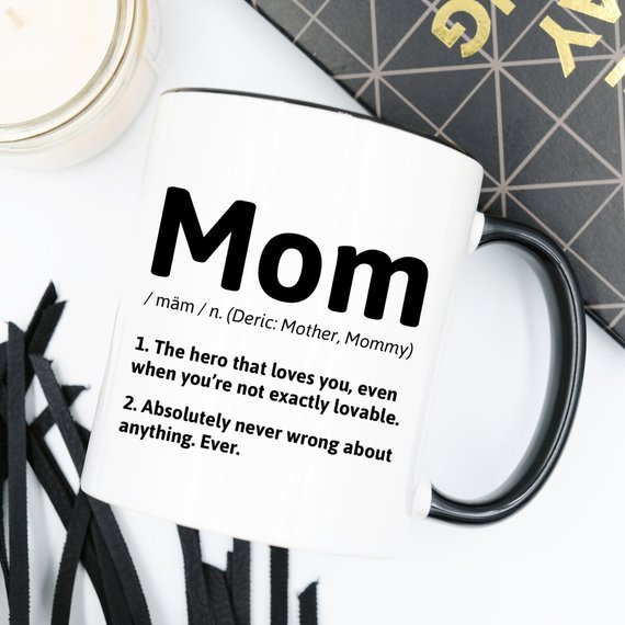 A white ceramic coffee mug featuring a humorous definition of 'Mom', perfect for gifts.