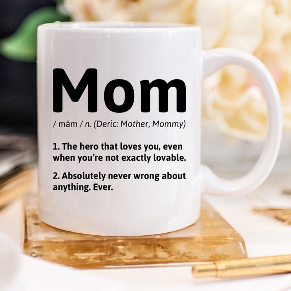 A white ceramic coffee mug featuring a humorous definition of 'Mom', perfect for gifts.