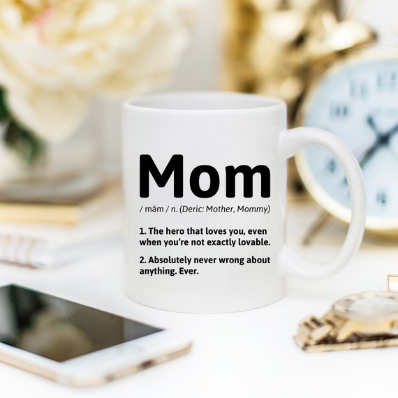 A white ceramic coffee mug featuring a humorous definition of 'Mom', perfect for gifts.