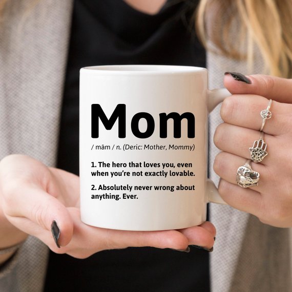 A white ceramic coffee mug featuring a humorous definition of 'Mom', perfect for gifts.