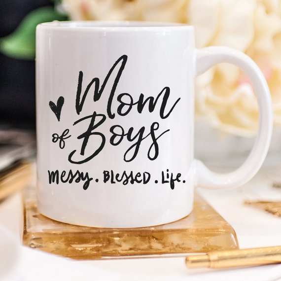 A ceramic coffee mug with the phrase 'Mom Of Boys. Messy. Blessed. Life.' printed in a playful font, showcasing a fun and relatable design for mothers.