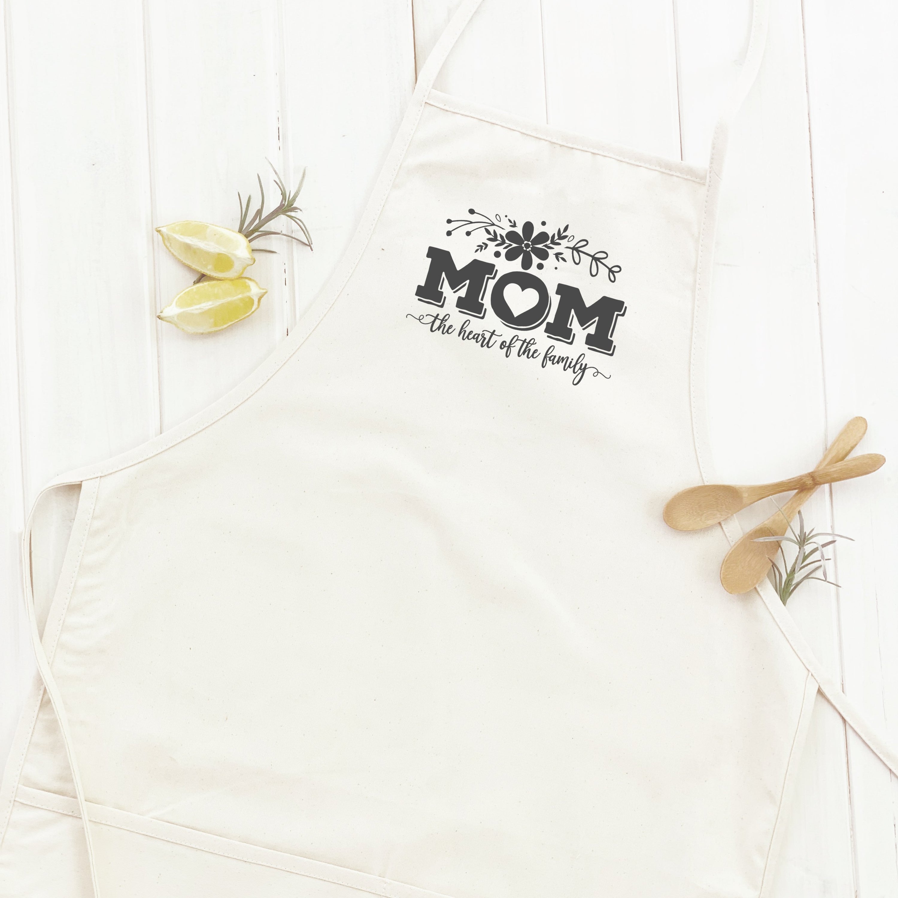 A stylish women's apron featuring the phrase 'Mom the Heart of Family', made from durable cotton canvas with a divided front pocket.