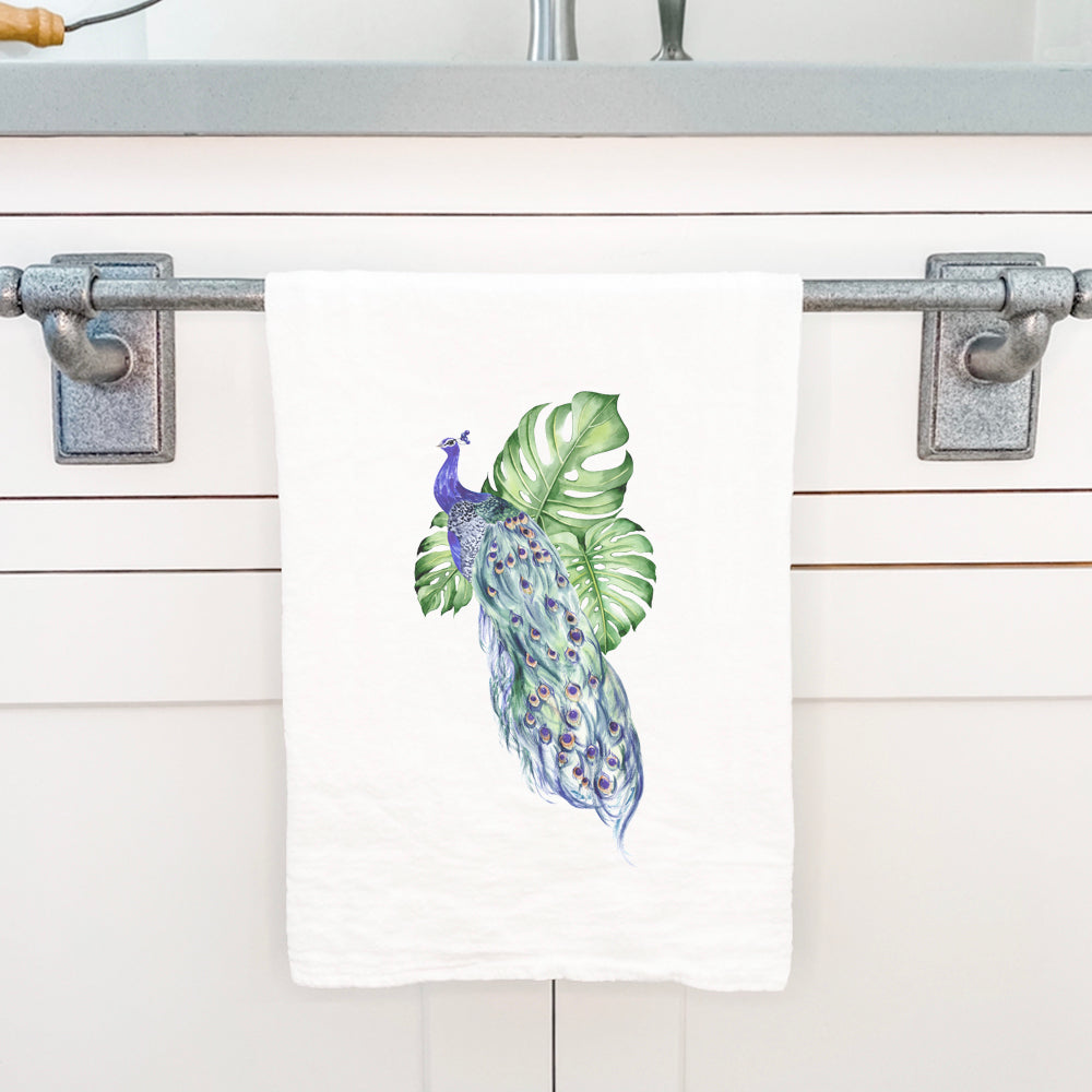 A vibrant cotton tea towel featuring a peacock and monstera leaf design, perfect for kitchen use.