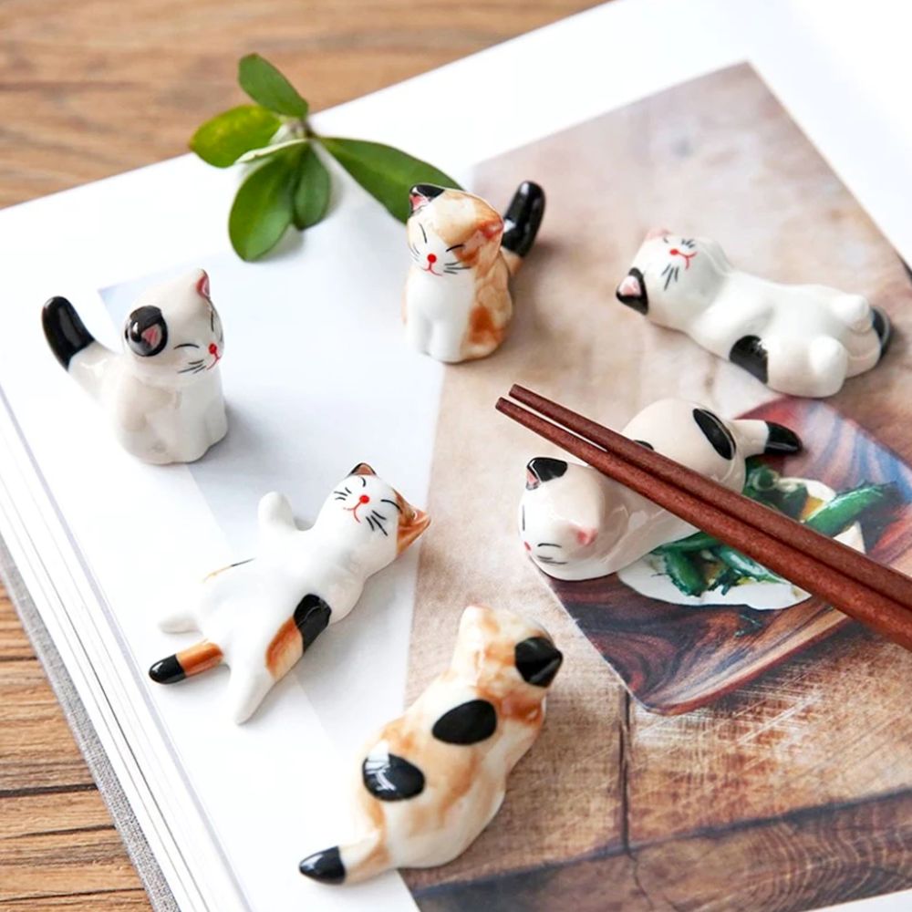 A set of six porcelain cat chopstick holders in various adorable poses, perfect for dining decor.