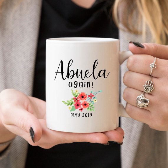 A charming white ceramic mug featuring a vibrant design celebrating Abuela, perfect for coffee or tea.