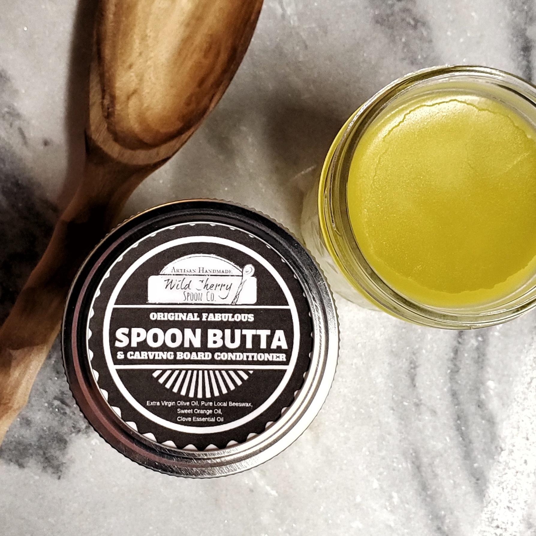 A 4 oz jar of Spoon Butta wood conditioner with a wooden spoon and cutting board in the background, showcasing its natural ingredients.