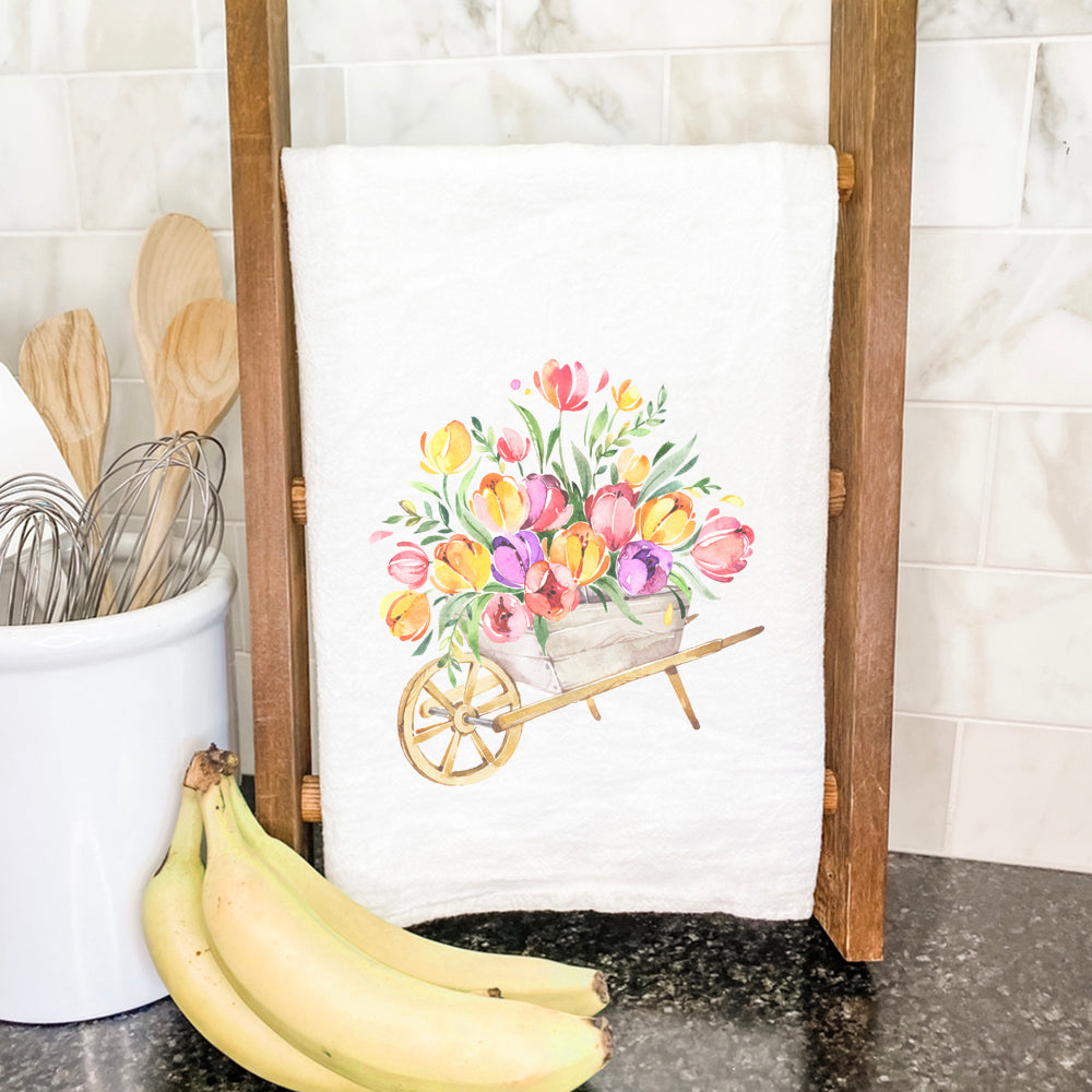 A colorful cotton tea towel featuring a spring floral wheelbarrow design, showcasing vibrant colors and hemmed edges.