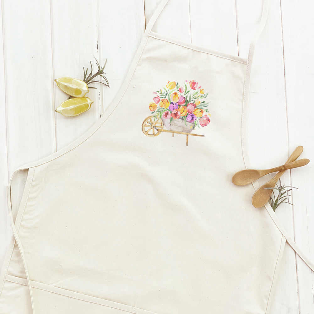 A stylish women's apron featuring a spring floral wheelbarrow design, made from durable cotton canvas with natural twill ties.