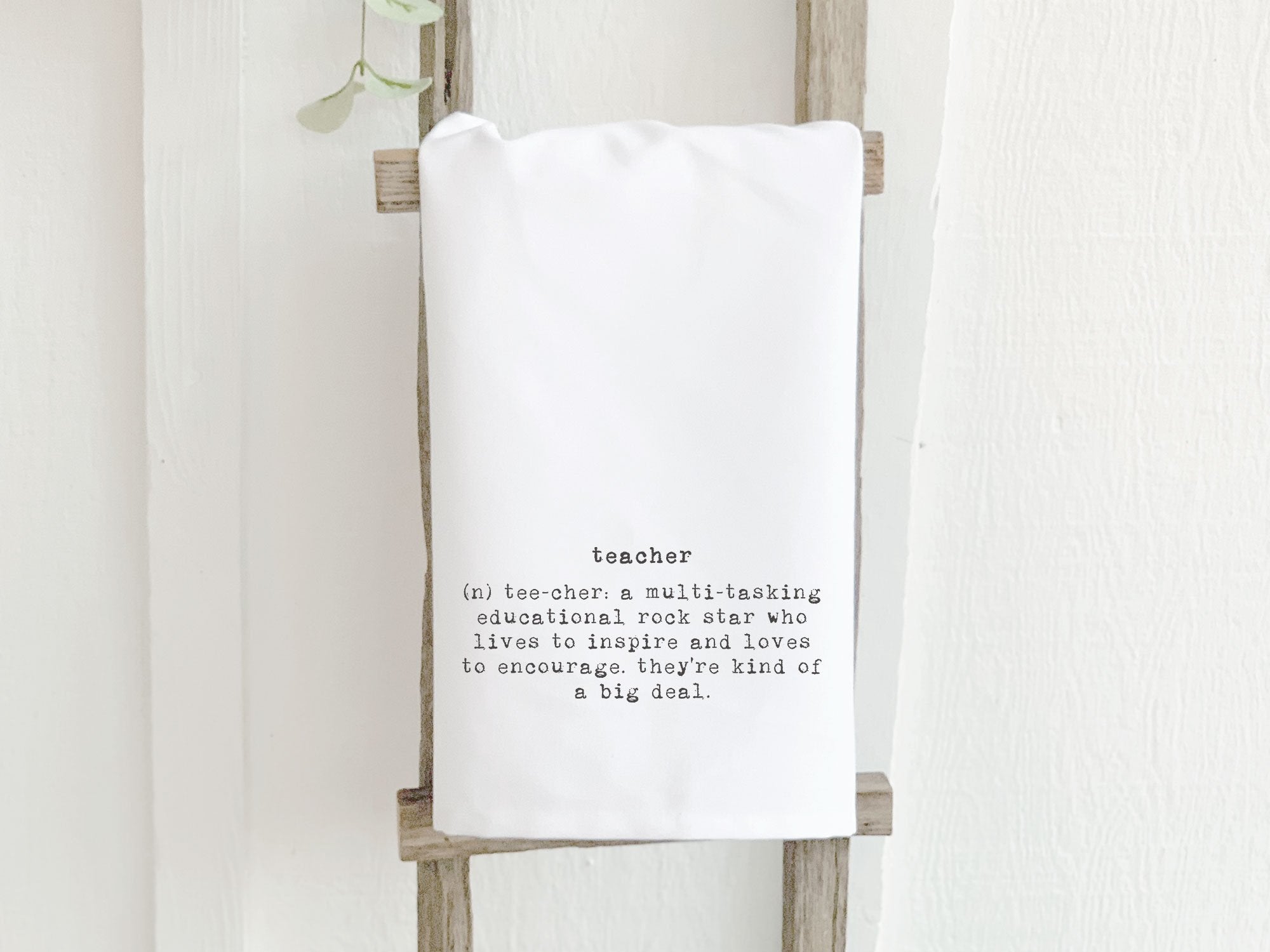 A vibrant cotton tea towel featuring the definition of a teacher, designed with water-based inks and hemmed edges, measuring 27 inches square.