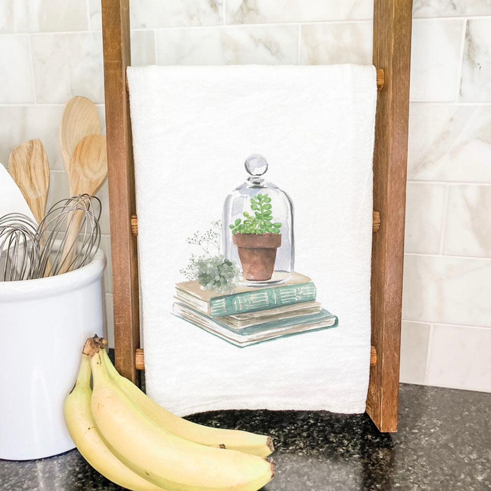 A vibrant cotton tea towel featuring a terrarium and books design, perfect for kitchen use.