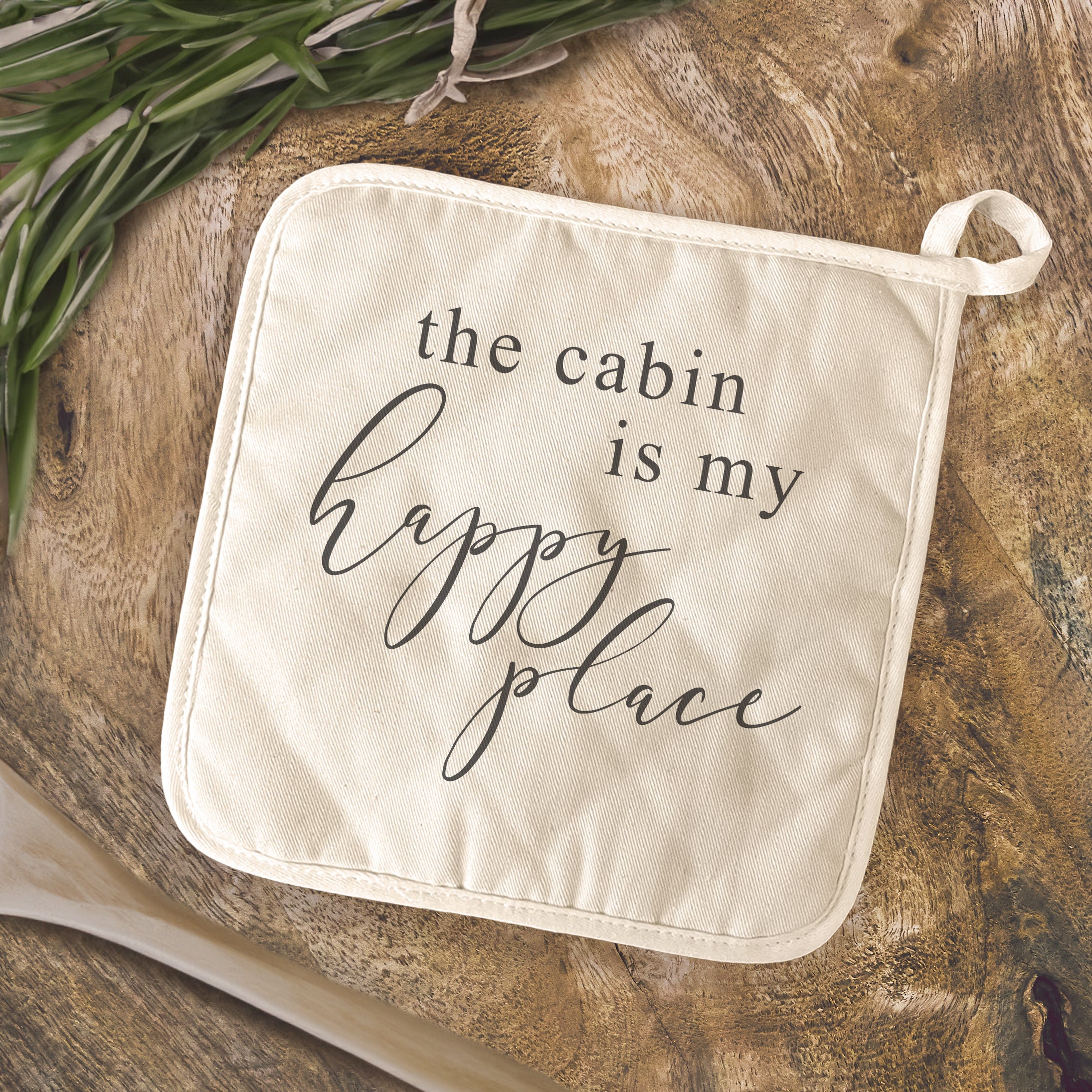 Cotton pot holder featuring 'The Cabin is my Happy Place' design, showcasing vibrant colors and a convenient hanging loop.