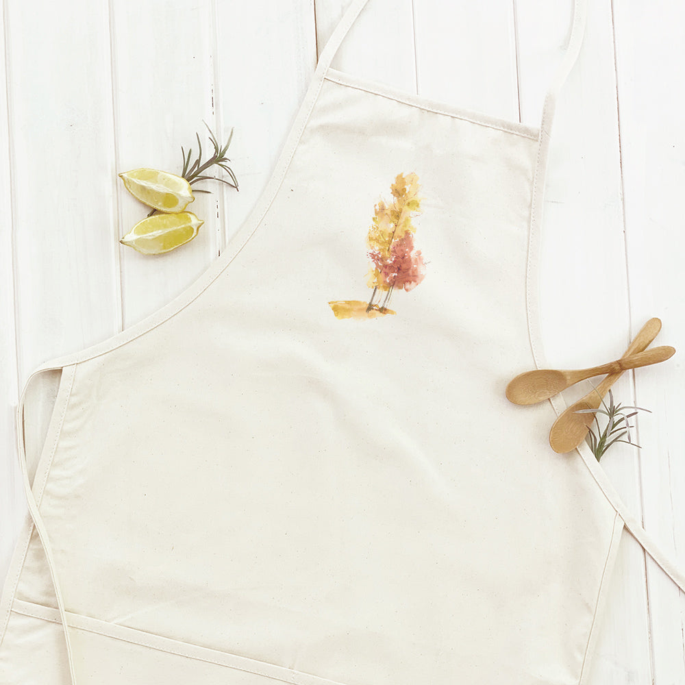 A stylish women's apron featuring a watercolor design of fall trees, made from durable cotton canvas with natural twill ties.