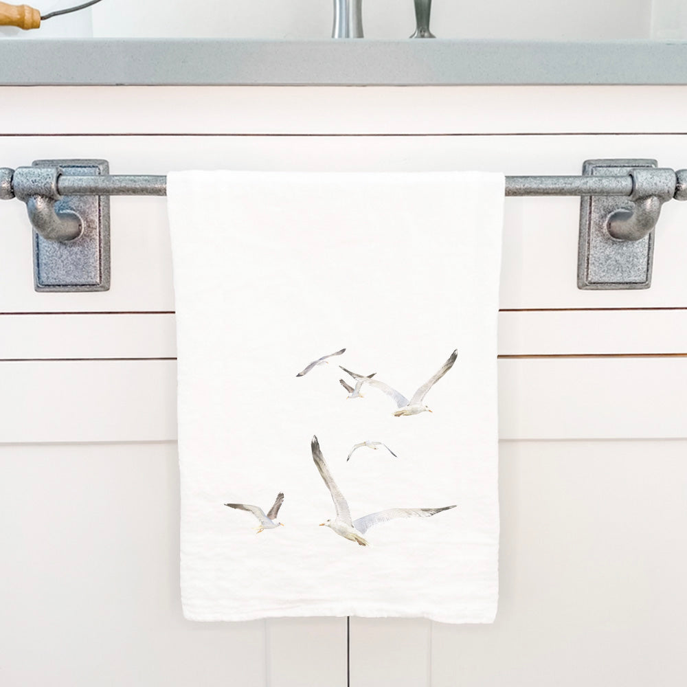 A vibrant cotton tea towel featuring watercolor flying seagulls design, perfect for kitchen use.