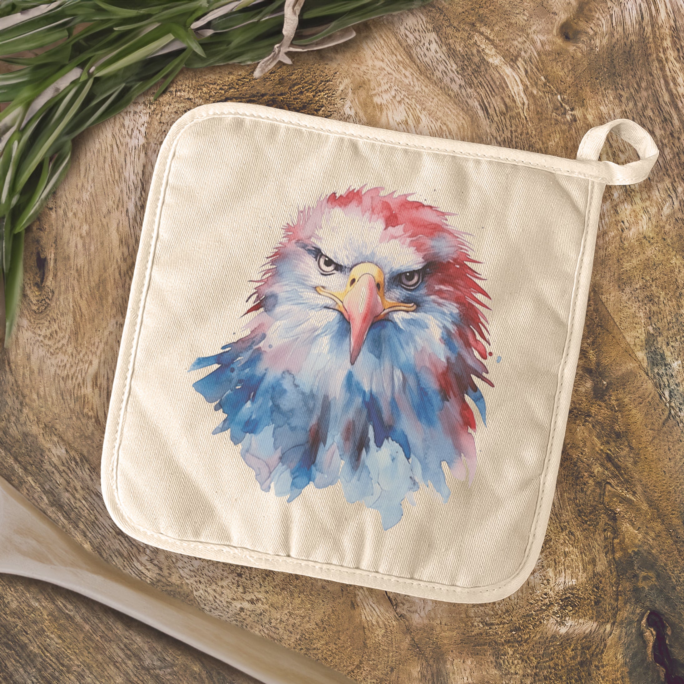 A vibrant watercolor design of a patriotic eagle on a cotton pot holder, showcasing its square shape and hanging loop.