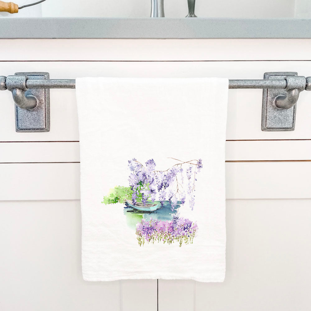 A vibrant cotton tea towel featuring a watercolor pond scene with a boat, showcasing lush greenery and serene water.