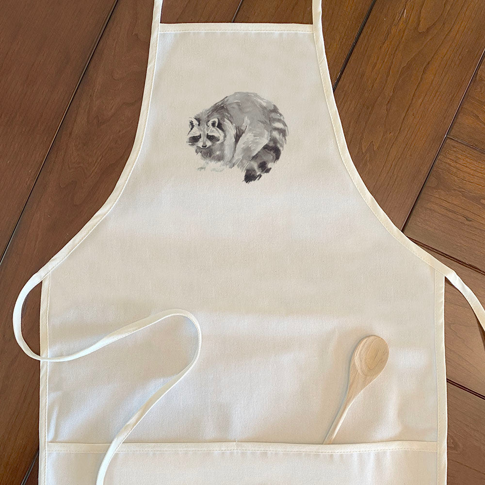 A stylish women's apron featuring a watercolor raccoon design, made from durable cotton canvas with adjustable neck and twill ties.