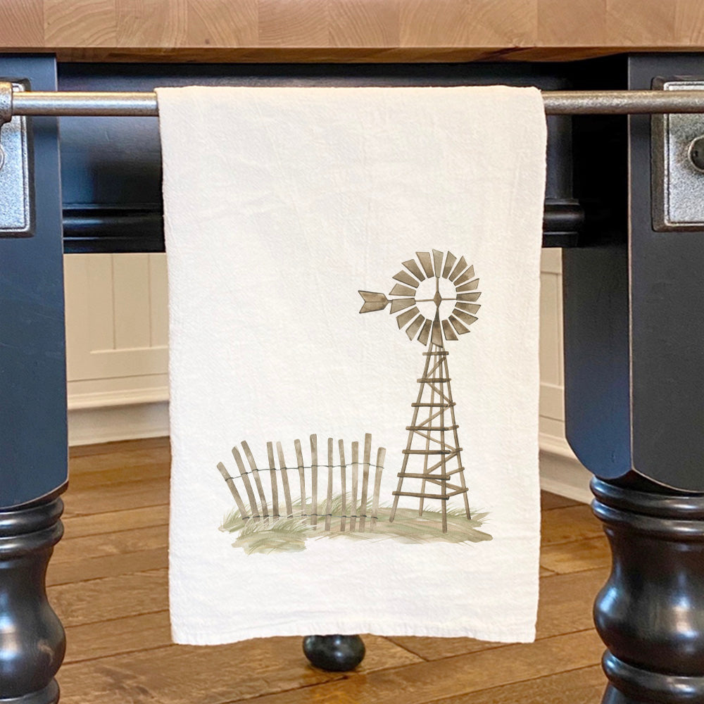 A vibrant cotton tea towel featuring a watercolor weathervane scene, showcasing its absorbent texture and hemmed edges.