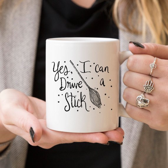 A humorous coffee mug featuring the phrase 'Yes I Can Drive A Stick', perfect for Halloween and coffee lovers.