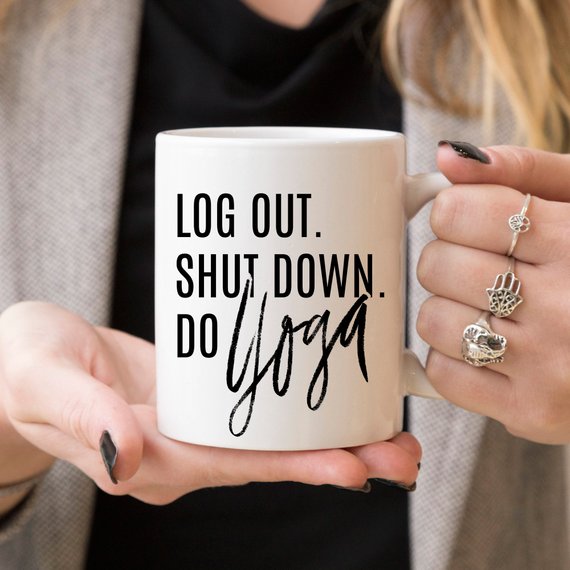 A humorous Yoga Mug with the phrase 'Log Out, Shut Down. Do Yoga' printed on it, showcasing its ceramic design and 11 oz capacity.