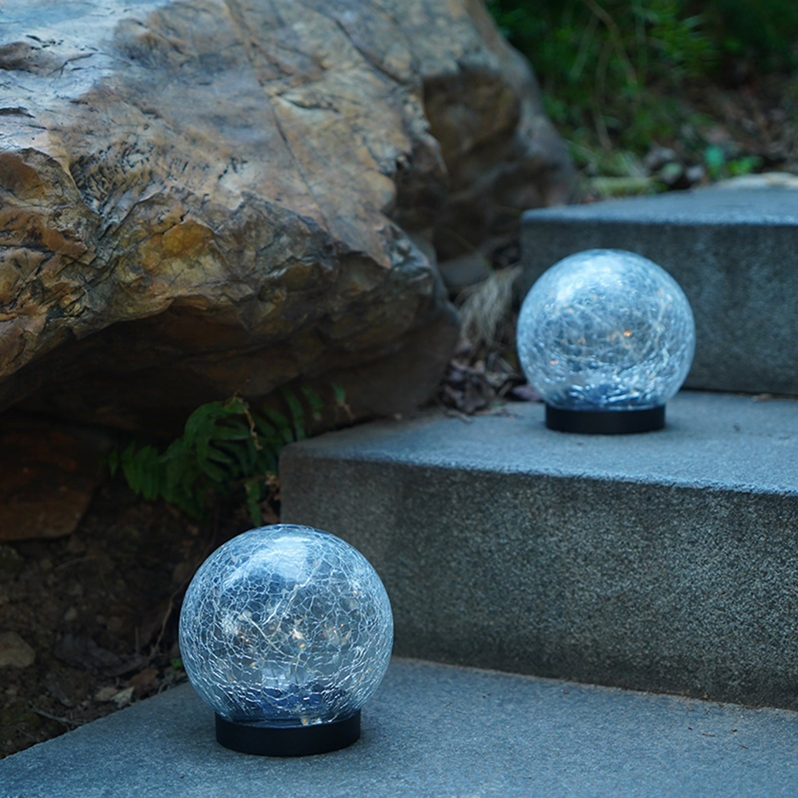 Two solar lights with cracked glass ball design illuminating a garden path at night, showcasing warm LED light patterns.