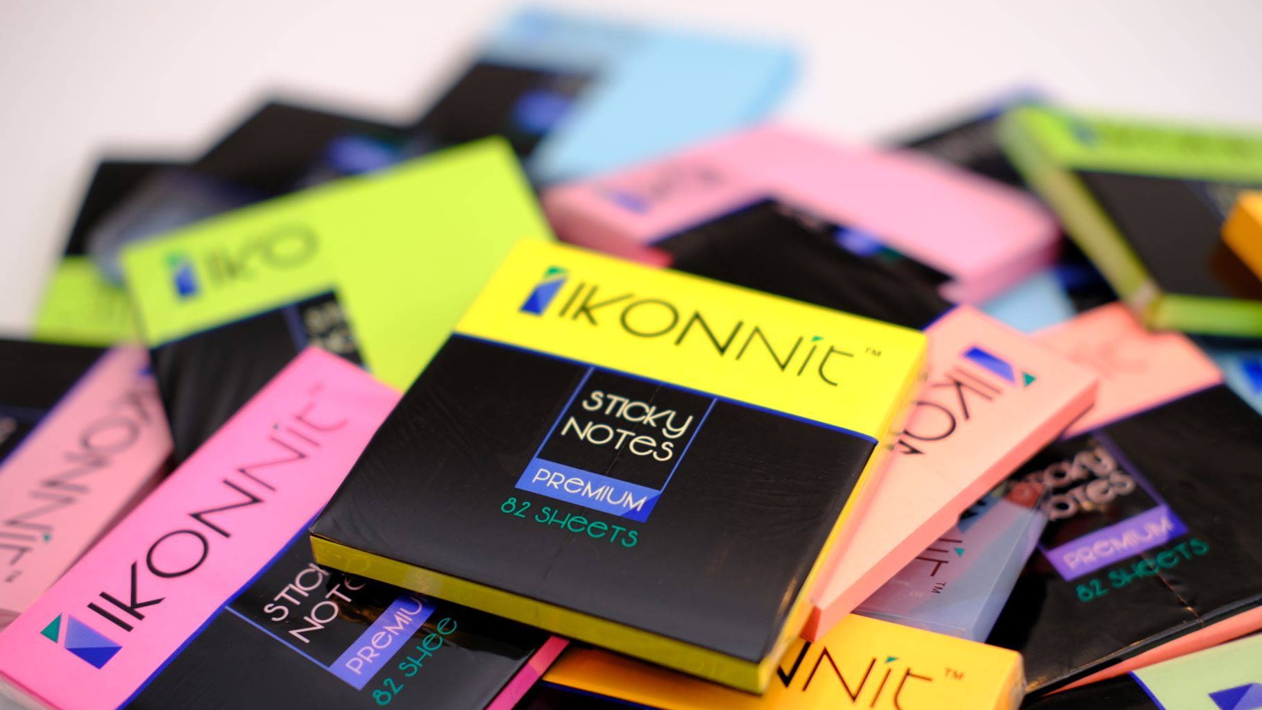 A vibrant assortment of 12 pack 3x3 self-stick sticky notes in various bright colors including pink, blue, yellow, green, orange, magenta, and purple, displayed on a clean desk.