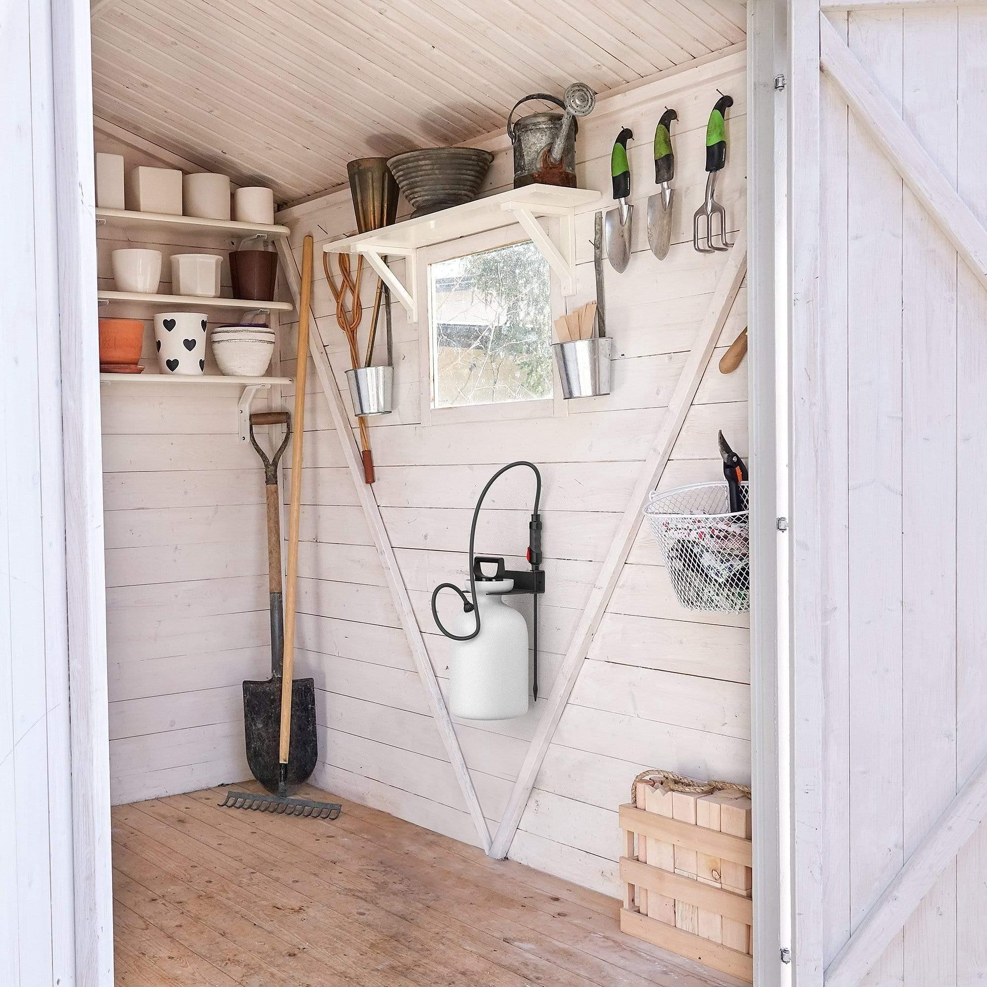 A wall-mounted garden sprayer holder made of heavy gauge steel, featuring a black powder-coated finish, securely holding a pressure sprayer in a garage setting.