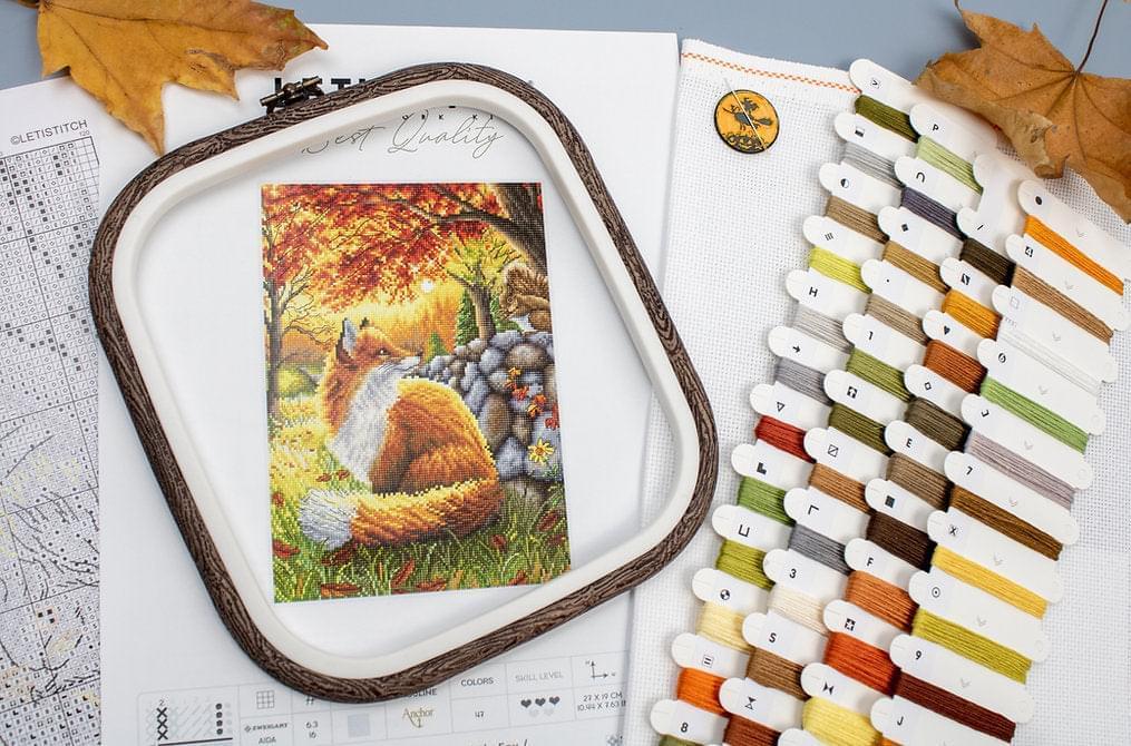 A counted cross stitch kit featuring a friendly fox design, including Aida canvas, colorful threads, and a needle.