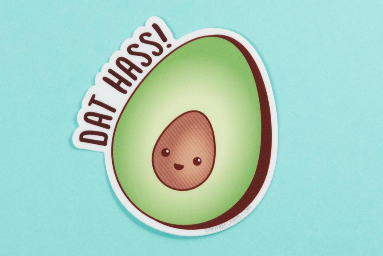 A colorful vinyl sticker featuring a happy avocado with the pun 'Dat Hass!' in playful lettering.