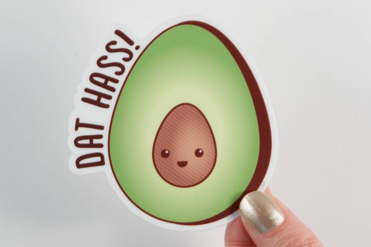 A colorful vinyl sticker featuring a happy avocado with the pun 'Dat Hass!' in playful lettering.