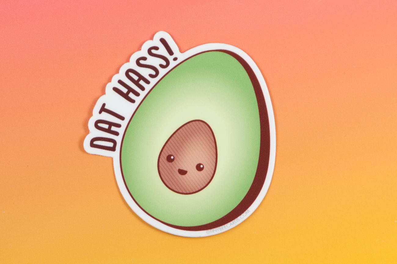 A colorful vinyl sticker featuring a happy avocado with the pun 'Dat Hass!' in playful lettering.