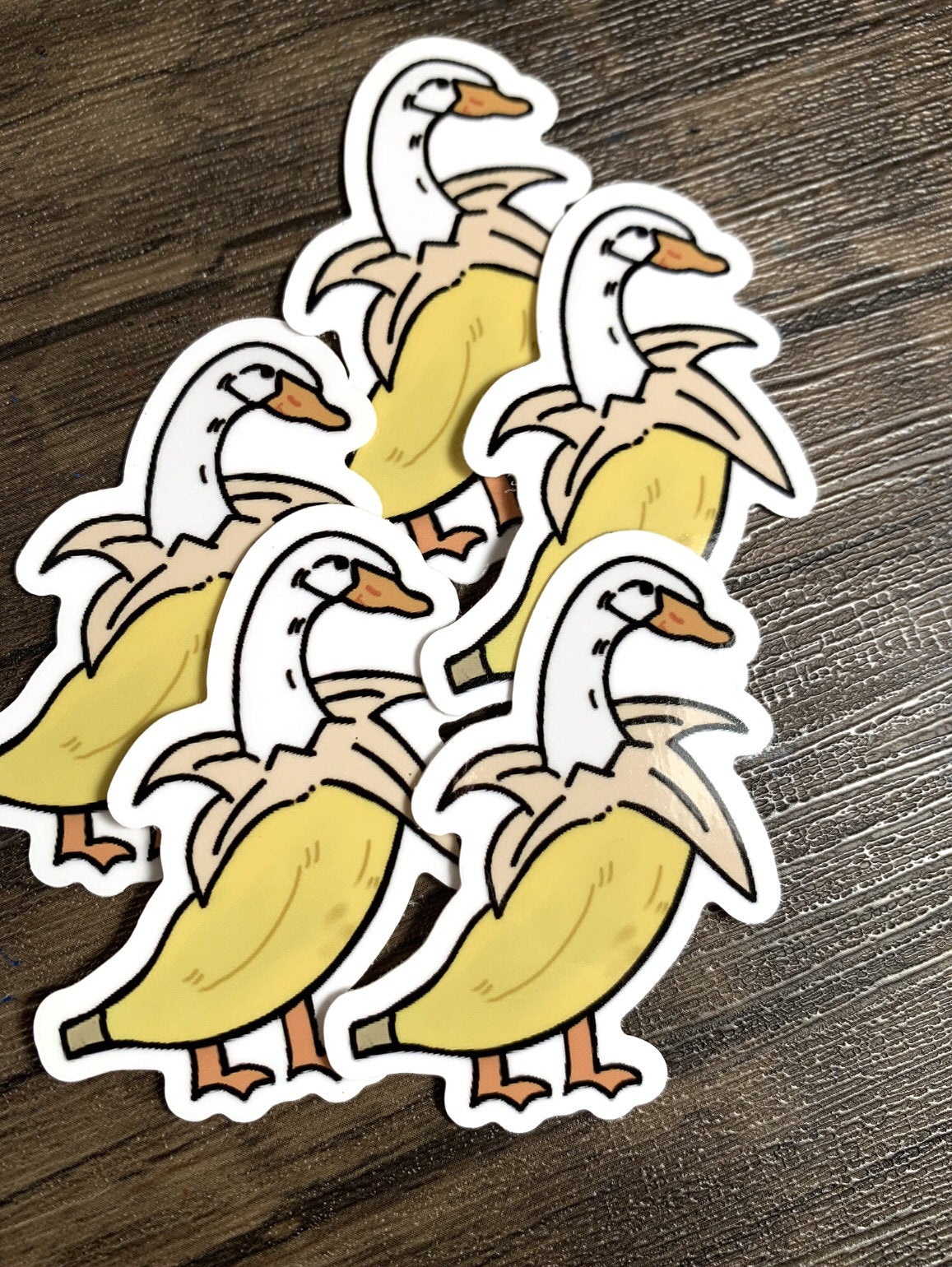 A cute banana duck sticker featuring a whimsical design, available in white and purple options, perfect for personalizing items.