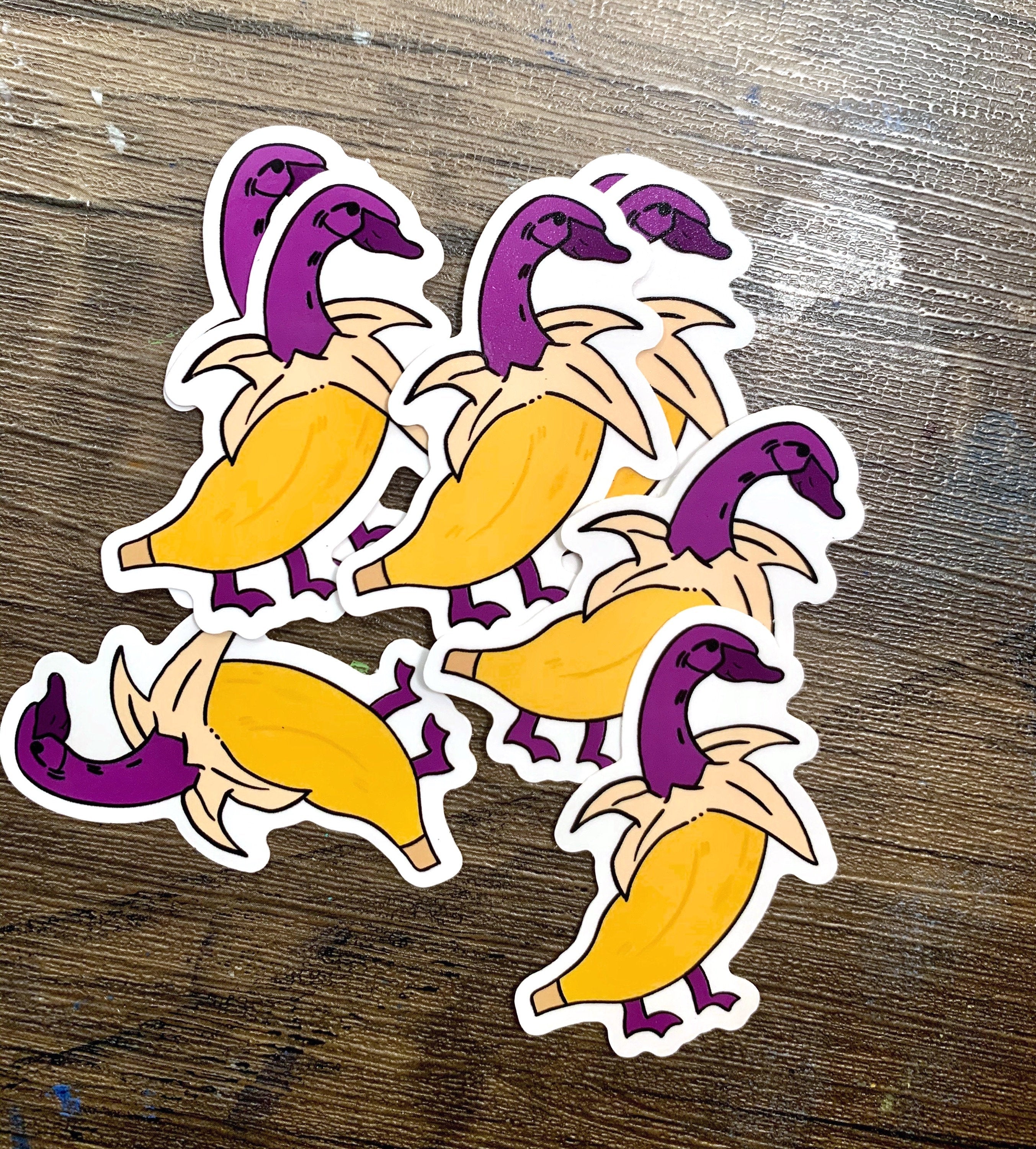 A cute banana duck sticker featuring a whimsical design, available in white and purple options, perfect for personalizing items.