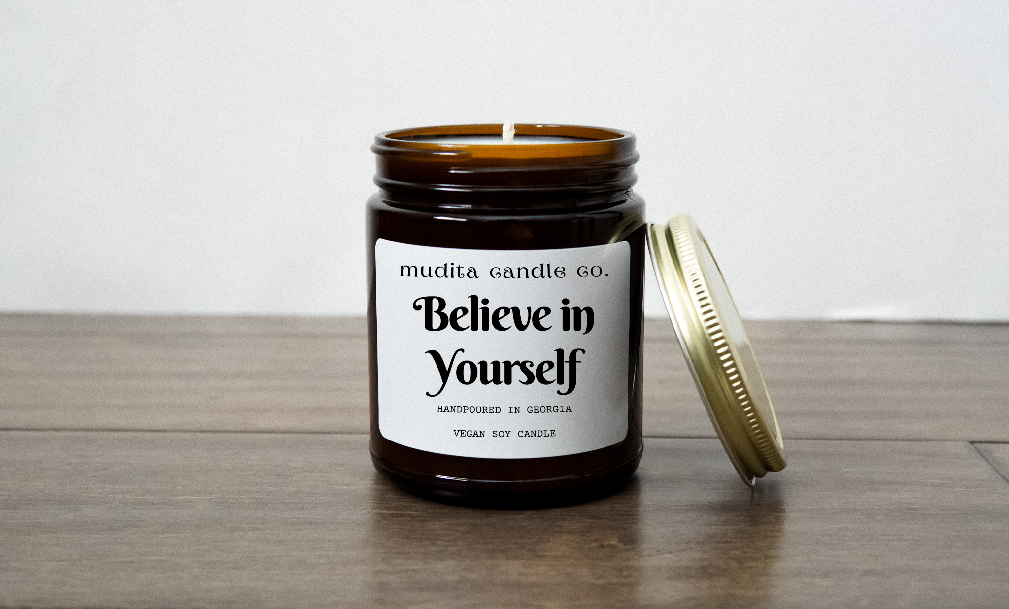 A beautifully crafted 'Believe in Yourself' candle in a 9oz amber glass jar with a gold metal lid, showcasing its elegant design.