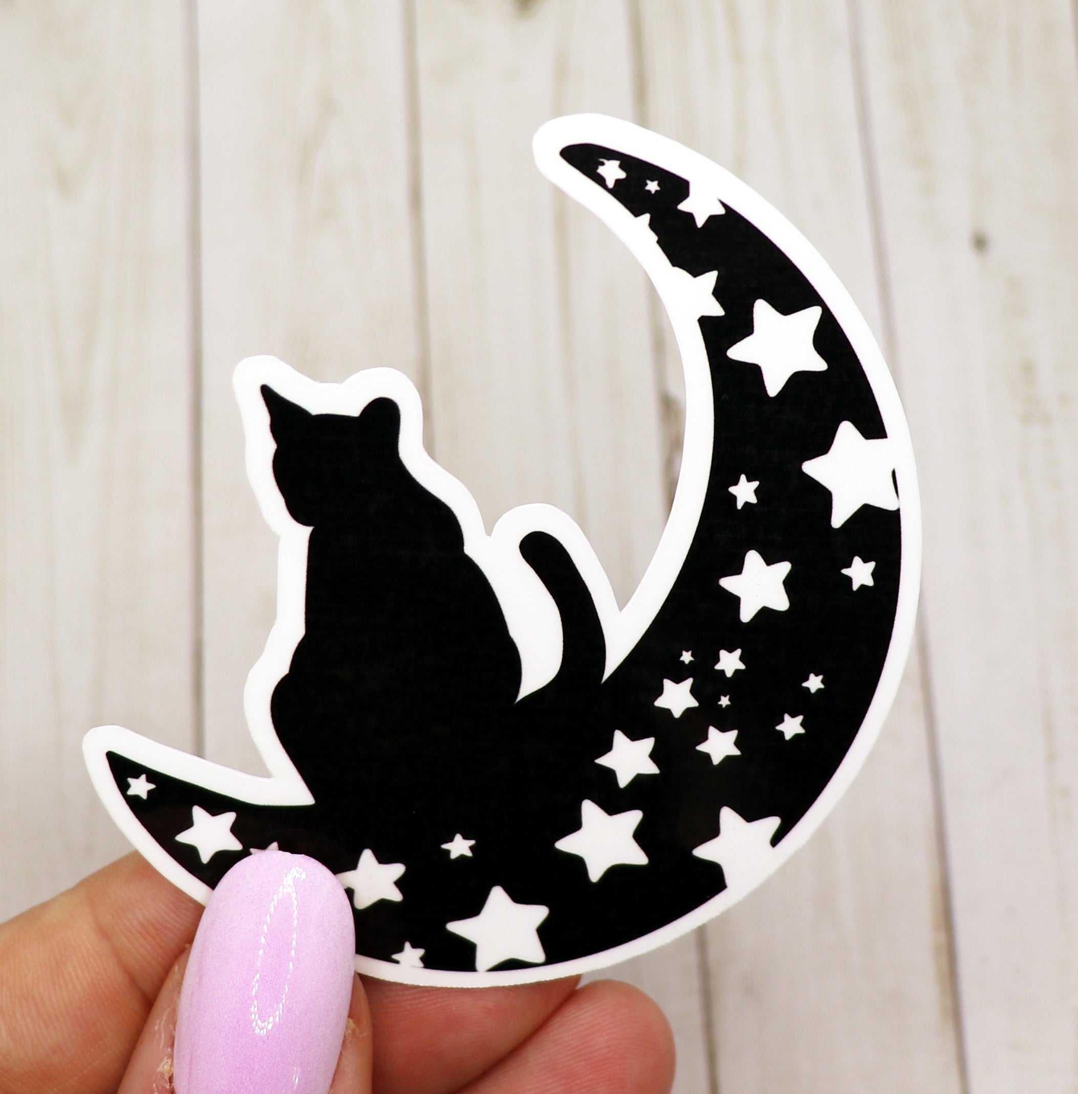 A vinyl sticker featuring a whimsical black cat sitting on a crescent moon against a starry background.