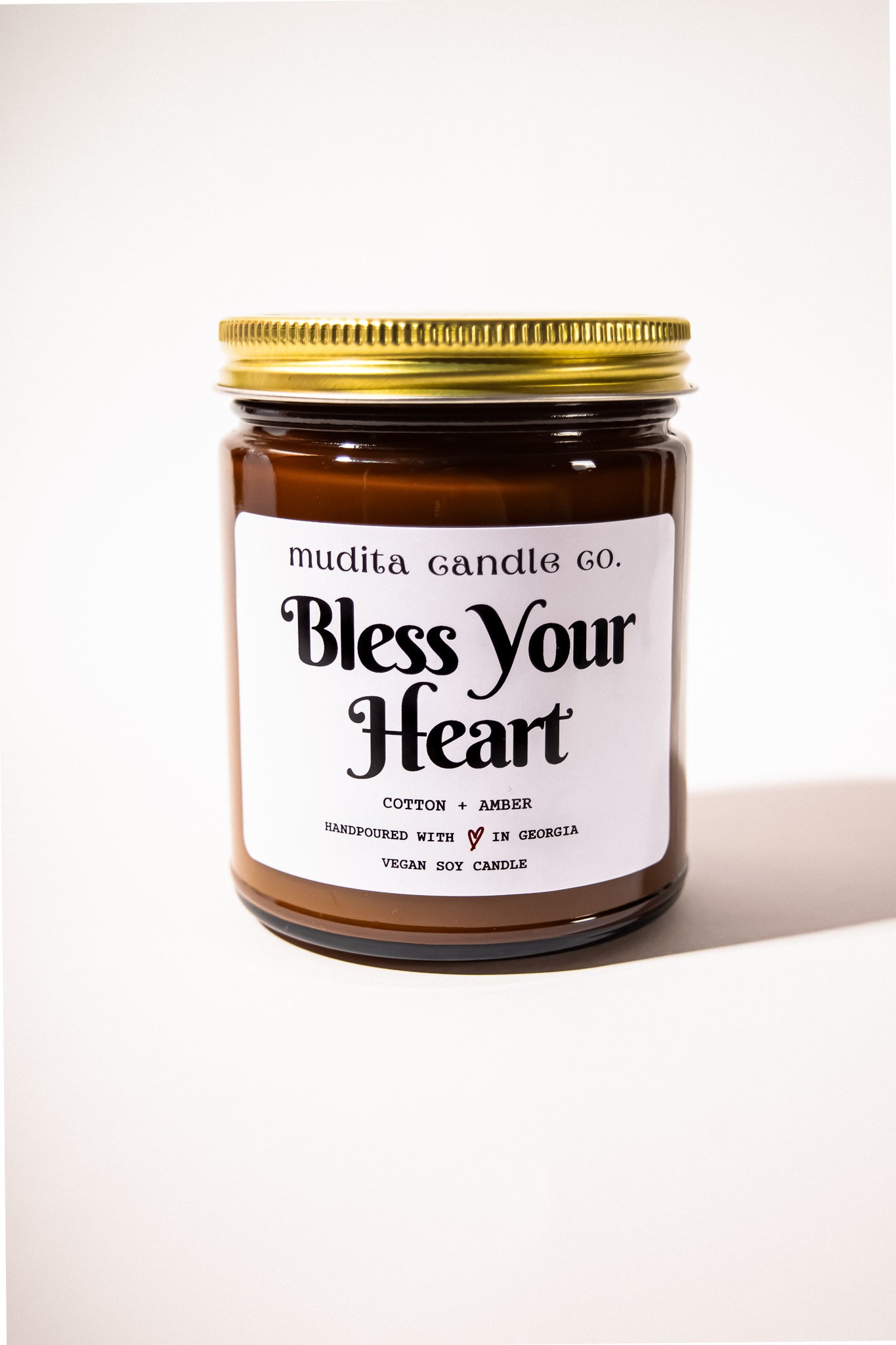 Bless Your Heart Cotton Amber Soy Candle in a reusable amber glass jar with a gold lid, showcasing its elegant design and inviting aroma.