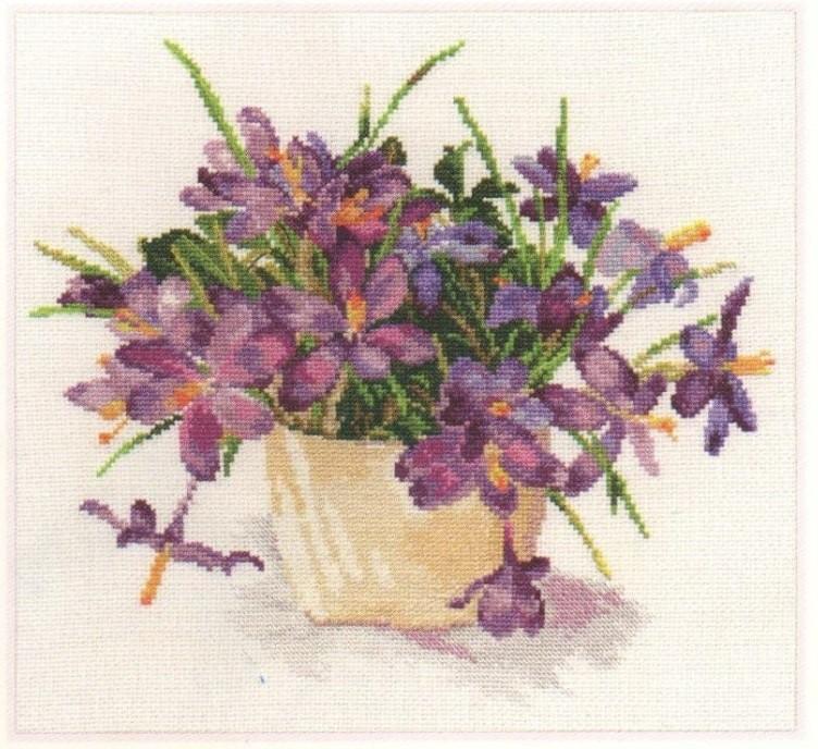 A beautifully arranged cross-stitch kit featuring crocuses, including white Aida fabric, colorful threads, and an embroidery needle.